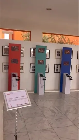 Row of colour-coded panels with listening stations along a gallery wall of framed photos.