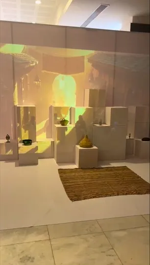 Projected medina scene behind white plinths displaying craft objects and a woven rug.