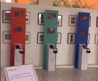 Exhibition hall with red, green and blue panels, each with a listening station and headphones.