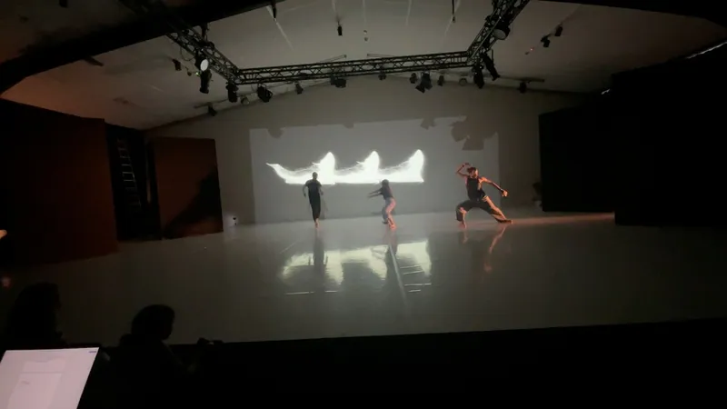 Wide view of a studio with two performers and a projected shape on the back wall.