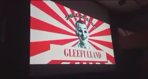 Title card on screen: a smiling face on red and white rays with the word GLEEFULLAND.