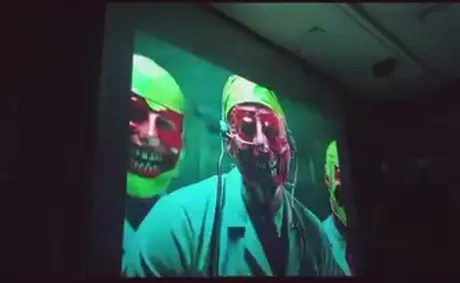Projected frame of masked figures in green light.