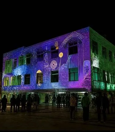 Two-storey building washed in purple, blue and green mapped patterns at night.